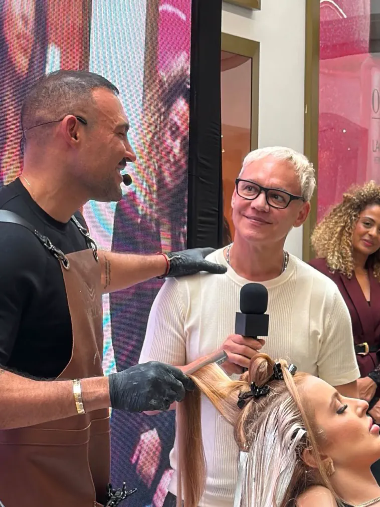 Edu Paiva, de microfone na mão, apresentando uma demonstração de coloração ao vivo em um evento da Wella